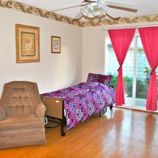 A cozy bedroom with a single bed and armchair, featuring bright pink curtains and decorative wall art.