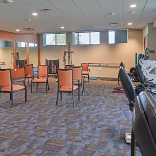 An empty gym with chairs arranged in a circle, mirrors on the walls, and a carpeted floor.