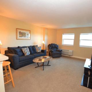 A cozy living room with a sofa, armchair, and coffee table, complemented by natural light from the windows.