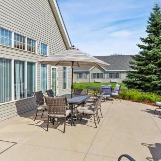 A sunny patio with tables and chairs set up for outdoor dining, adjacent to a residential building and garden.