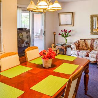 A cozy dining and living area featuring a wooden dining table with green placemats, a floral sofa, and decorative elements like flowers and artwork.