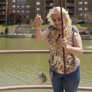 A woman fishing by a lake, holding her catch.