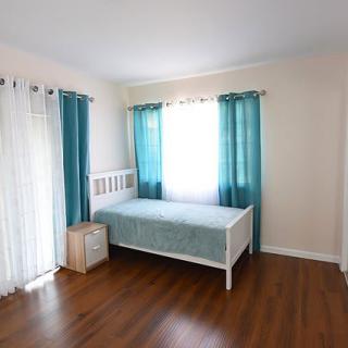 A minimalist bedroom with a daybed and teal curtains letting in natural light.