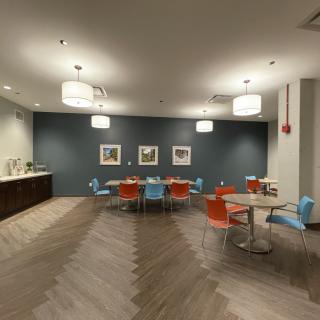 A modern office break room with colorful chairs and tables under warm lighting.