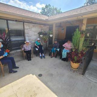 A group of people sitting and relaxing in a sunny courtyard surrounded by plants.