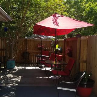 A cozy outdoor patio area with a red umbrella, surrounded by wooden fencing and shaded by trees.