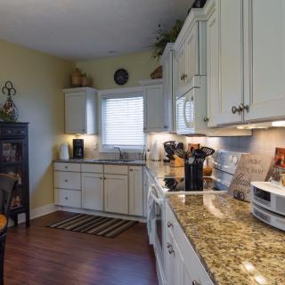 A modern kitchen with white cabinets and granite countertops, featuring a hardwood floor and various appliances.
