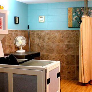 A cozy and organized laundry room featuring a washing machine, a small fan on a counter, tiled walls, and a curtain for separation.
