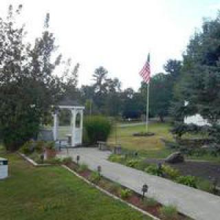 A serene outdoor garden with a pathway, gazebo, and flag surrounded by trees.