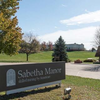 Entrance sign for Sabetha Manor with a building and landscaped grounds in the background.