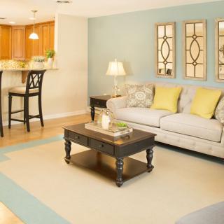 A cozy living room with a pastel color scheme, featuring a comfortable sofa and a stylish coffee table, open to an adjoining kitchen area.