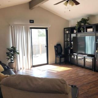 A cozy living room with a large television and ample natural light streaming in from the sliding door.
