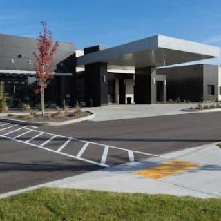 A modern building with a sleek design, featuring an entrance and adjacent parking lot on a clear day.
