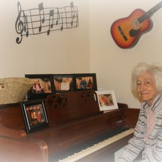 An elderly person sits by a piano in a room decorated with music notes and a guitar on the wall.