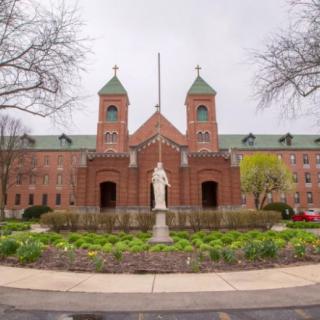 A brick church with twin towers and a statue in the foreground, surrounded by landscaped gardens.