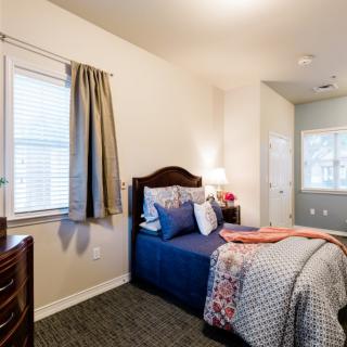 A cozy bedroom with a single bed, decorated with patterned bedding and pillows, next to a window with curtains.