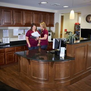 Two people working at a reception desk in an office setting.