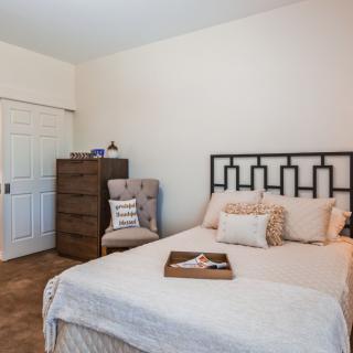 A cozy bedroom with a neatly made bed, dresser, and comfortable chair.