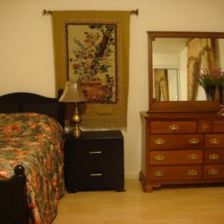 A cozy bedroom featuring a wooden bed with floral bedding, a matching dresser with mirror, and a decorative tapestry on the wall.