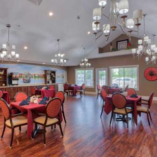 A beautifully decorated dining room with elegant chandeliers, featuring multiple tables and chairs set on a wood floor, with large windows providing natural light.