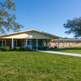 A welcoming single-story residential building surrounded by lush green grass and clear blue skies.
