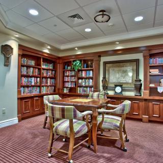 A cozy library space with wooden bookshelves and a round table surrounded by chairs.
