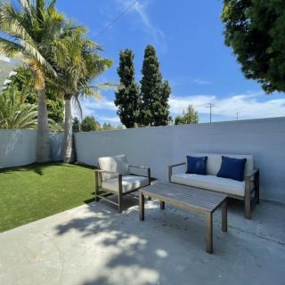 A cozy patio area with seating under a sunny blue sky, surrounded by greenery and palm trees.