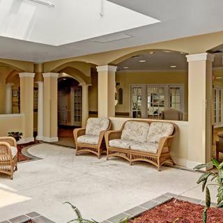 A spacious lobby area with wicker furniture and a skylight, surrounded by columns and decorative indoor plants.