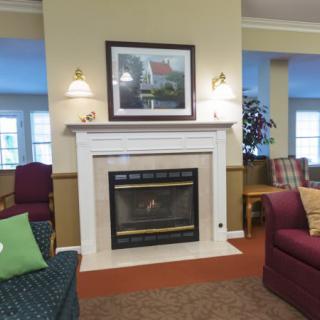 A cozy living room featuring a central fireplace surrounded by comfortable seating and artwork on the wall.