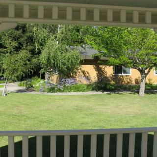 A view of a house and garden with trees and a well-maintained lawn, seen from a porch.