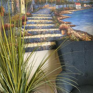 A cozy corner featuring a nature-themed painting with a pathway and coastal scenery, complemented by an indoor plant and a comfortable chair.