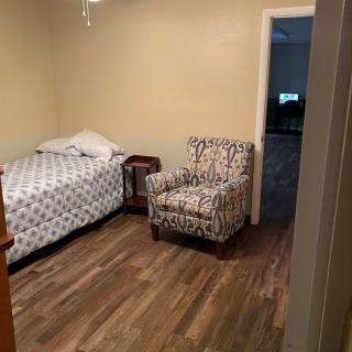 A simple bedroom with a single bed and patterned armchair.