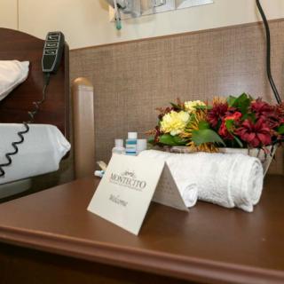 A hospital room with a bedside table featuring a bouquet of flowers, a towel, and a welcome card.