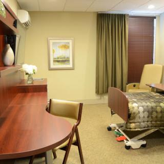 A well-appointed hospital room featuring a comfortable bed, desk, and decorative artwork.