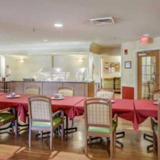A cozy dining room setup featuring tables with red tablecloths and a visible kitchen area.