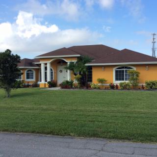 A suburban single-story house with a well-maintained lawn under a partly cloudy sky.