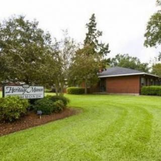 A small brick building surrounded by a lush green lawn and trees, with a sign visible in the foreground.