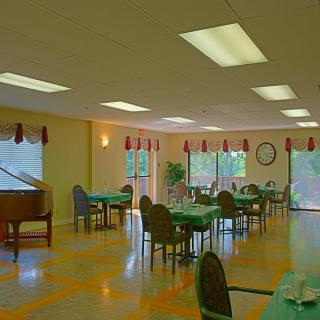 A spacious dining room with tables and chairs, featuring a piano and large windows.