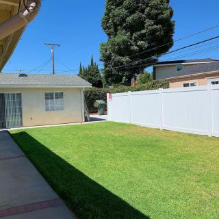A sunny backyard with a lawn, white fence, and patio area.
