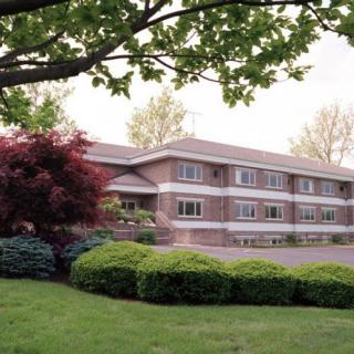 A two-story brick building surrounded by lush greenery and trees.