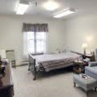 A neatly organized healthcare facility room with a single hospital bed and furniture.