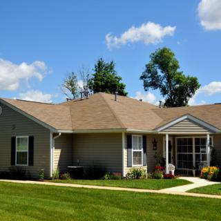 A single-story suburban house with a well-maintained lawn under a blue sky with clouds.