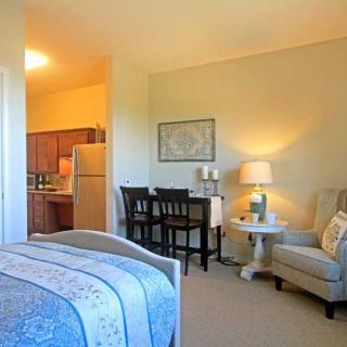 A cozy bedroom with an adjacent living space and kitchen, featuring comfortable seating and warm lighting.