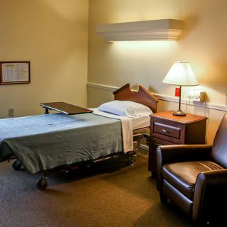 A hospital room with a bed, lamp, and comfortable chair.