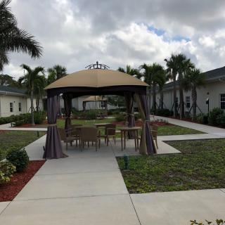 An outdoor area featuring a gazebo surrounded by palm trees and a walkway under a cloudy sky.