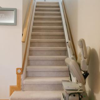 A carpeted staircase with a stairlift installed for accessibility.