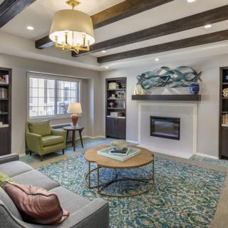 A stylish living room featuring a sofa, armchair, and fireplace with decorative ceiling beams and bookshelves.