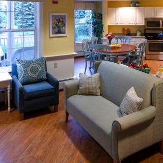A cozy living room and kitchen area featuring a sofa, armchair, dining table, and bright decor.