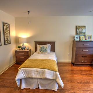 A cozy bedroom with a single bed, wooden floor, and warm lighting.