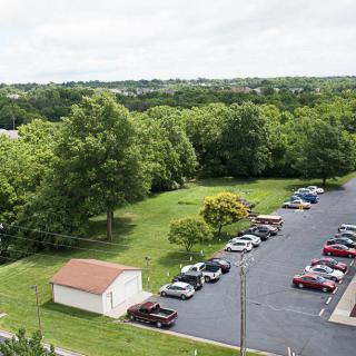 Aerial view of a parking lot adjacent to a green, tree-filled landscape.